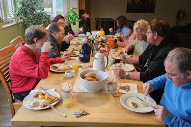 Mehrere Bewohner sitzen an einem Tisch und nehmen Mahlzeiten zu sich.