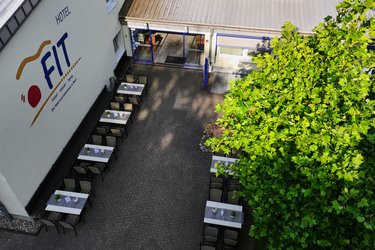 Das Hotel Fit ist aus der Luft zu sehen. Draußen befindet sich eine Terrasse mit Tischen, am Haus ist das Logo sichtbar.