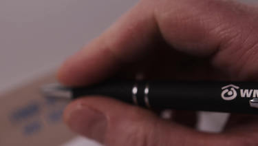 Nahaufnahme einer Hand mit Stift, auf dem das WMB-Logo sichtbar ist